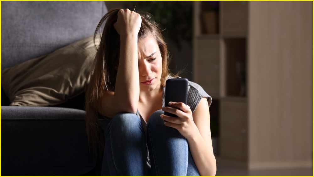 Frightened woman looking at a phone screen with tears rolling down her face.