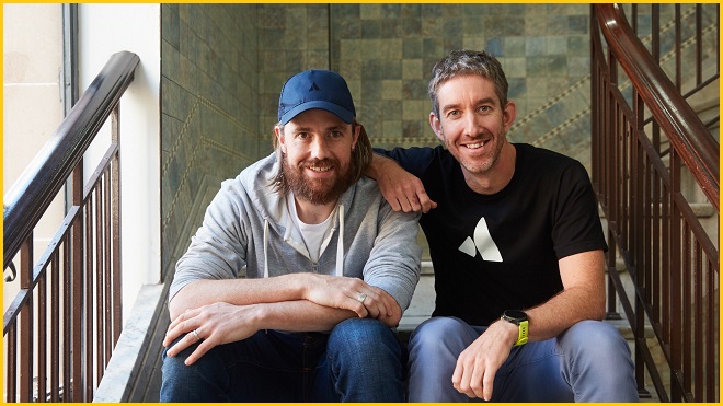 Atlassian founders Mike Cannon-Brookes and Scott Farquhar sit on a staircase.
