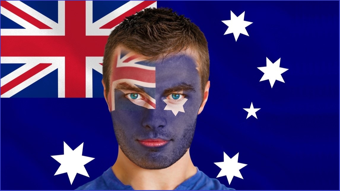 Man with an Australian flag face-painted on his face standing in front of an Australian flag