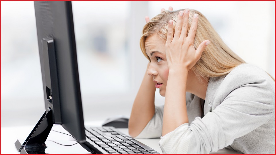 A woman with her head in her hands while she sits at a computer desk.