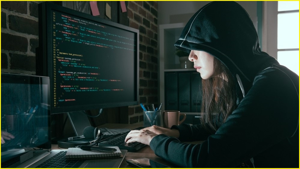female in black hoodie typing on computer screen