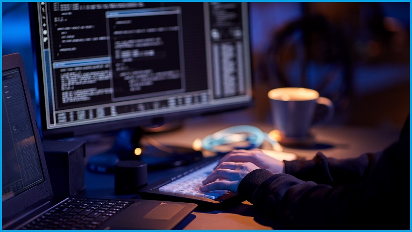 A hacker typing onto a dark computer screen.