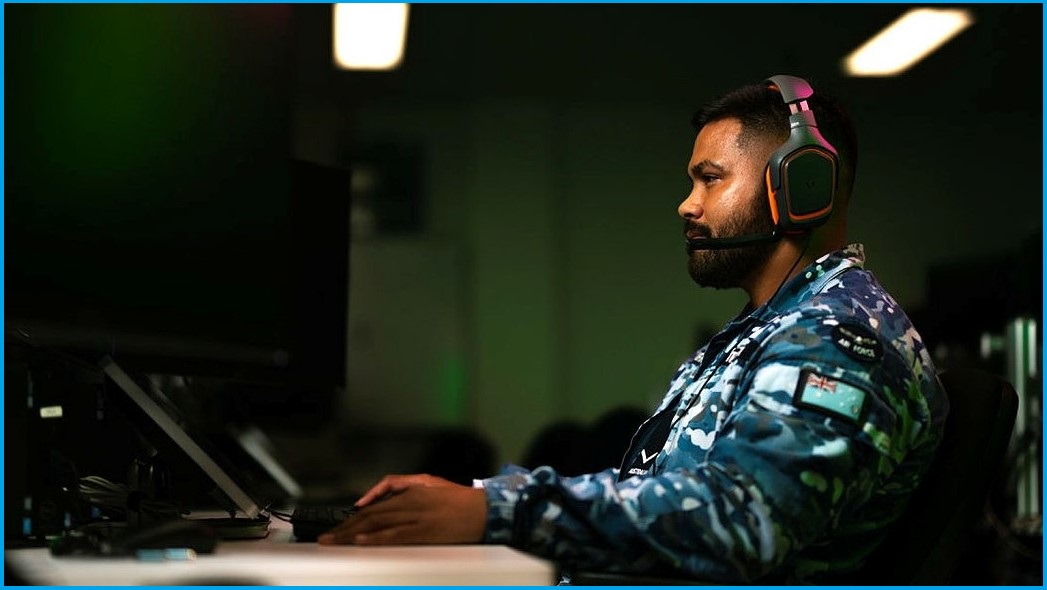 An airman sits at a computer with headphones on.