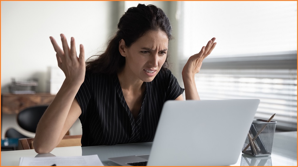 A woman at her laptop holding her hands up in frustration.