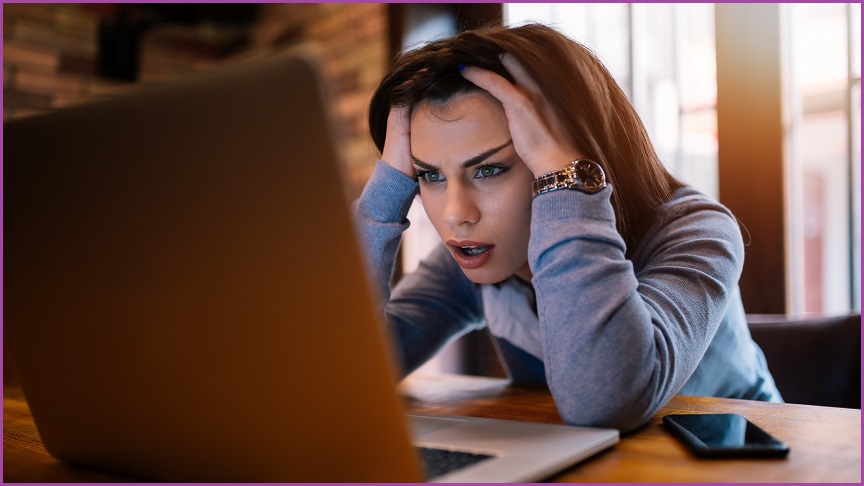 A woman sitting at a laptop screen looking frustrated.