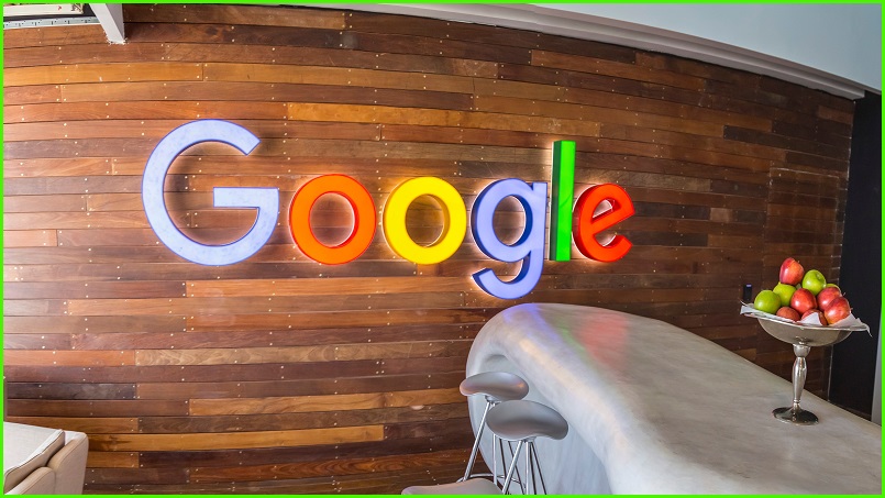 A Google sign in front of a countertop on which sits a bowl of apples.