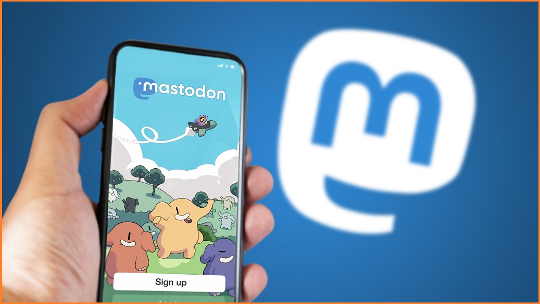 A hand holding up a phone of the Mastodon login screen in front of the Mastodon logo.