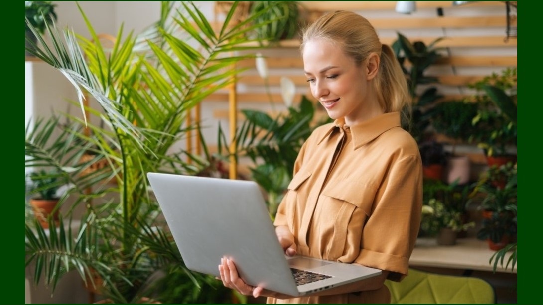A woman typing on a laptop surrounded by plants.