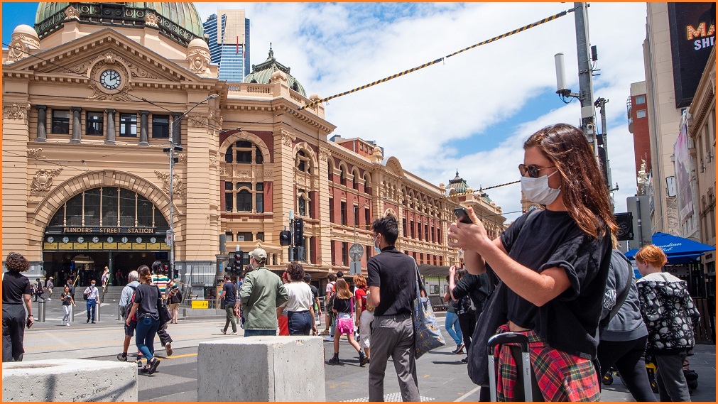 A woman wearing a mask standing outside Flinders Street Station.
