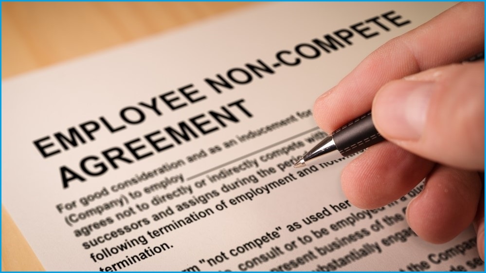 Person's hand signing non-compete agreement