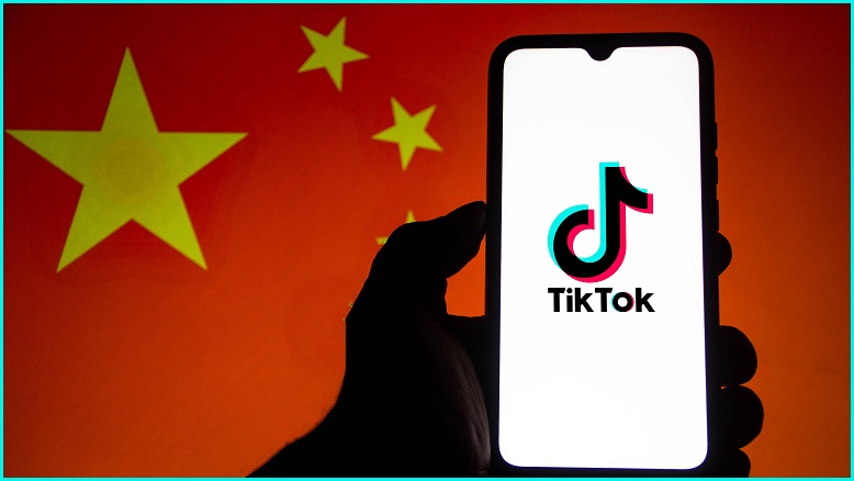 A hand in silhouette holding up a phone with the TikTok logo in front of a Chinese flag.