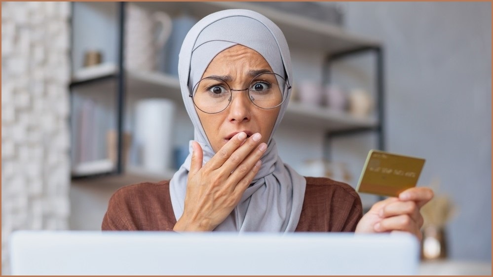 shocked woman holding credit card while looking at computer screen 
