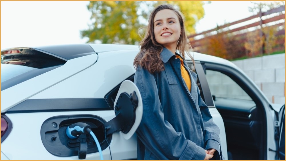 Smiling woman standing next to a charging electric vehicle