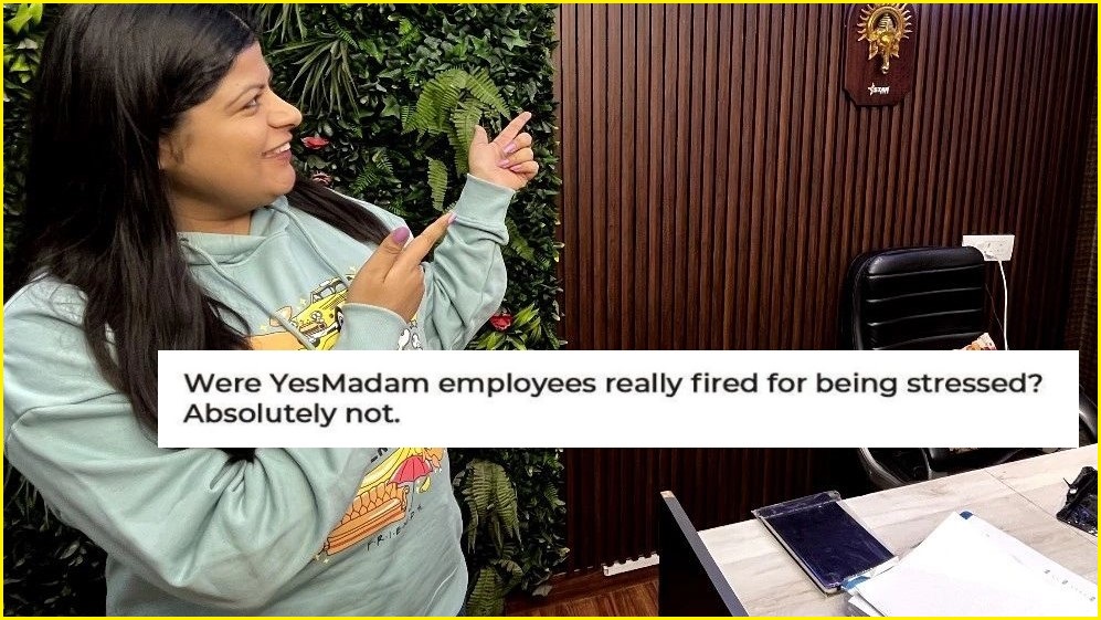 A medium shot of a woman with long hair standing next to a desk and pointing and smiling at the other side of the room, overlaid with text that reads "were YesMadam employees really fired for being stressed? Absolutely not."