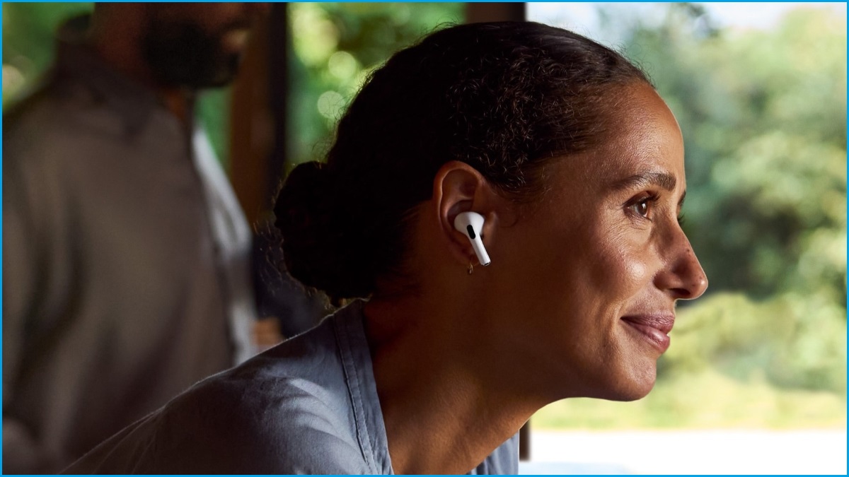 A close up of a woman of colour smiling slightly and wearing Apple AirPods in her ears.