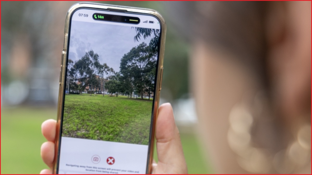 A close up of a hand holding a smartphone in a park, while the device live streams video of the park.