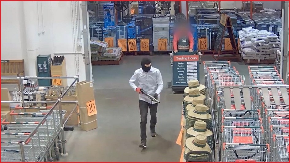 A man wearing a balaclava walking into a Bunnings store holding a shotgun.