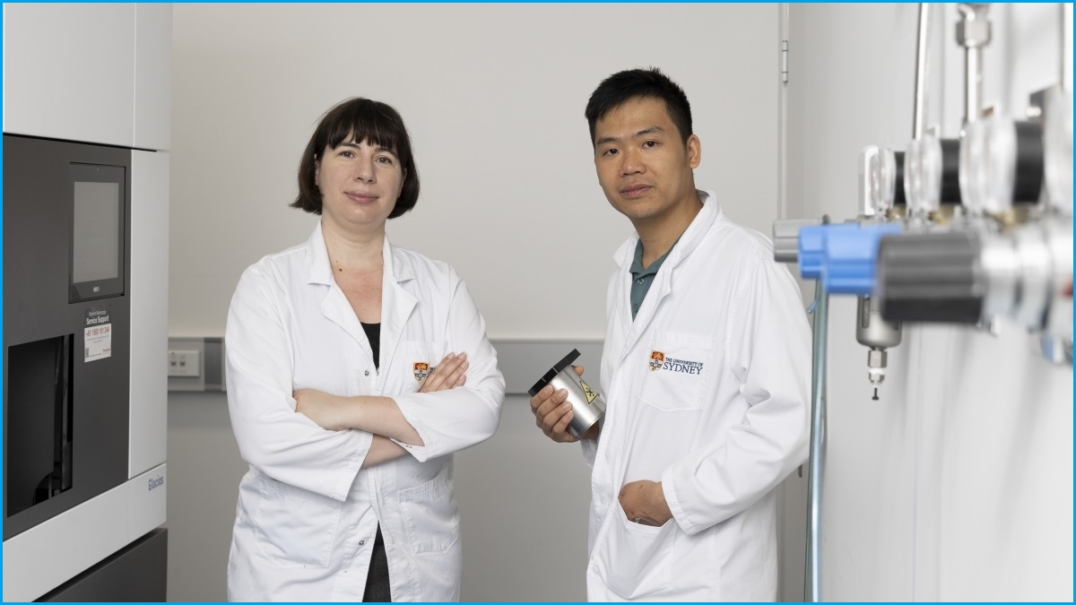 A medium shot of a woman and a man, both in scientists' white suits, standing in a lab.