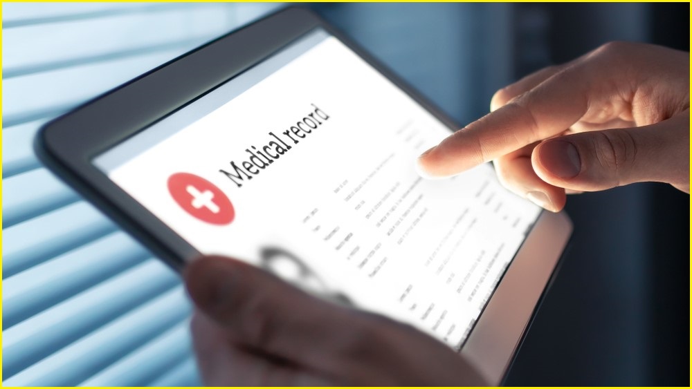 A close up of a person's hands holding a tablet and examining a digital medical record.