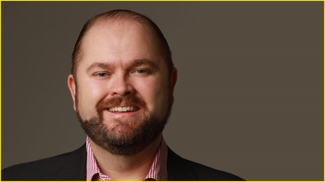 A close up of a middle-aged white man with a light beard smiling.