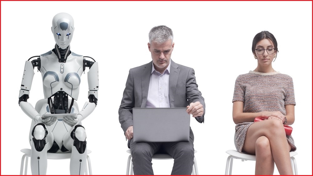 A man and a woman sit in chairs wearing business attire. A robot sits in a chair next to them.