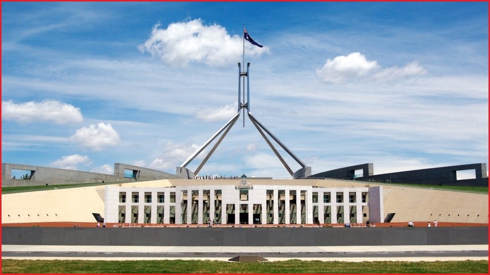 A wide exterior shot of Parliament House in Canberra, with clouds in the sky in the background.