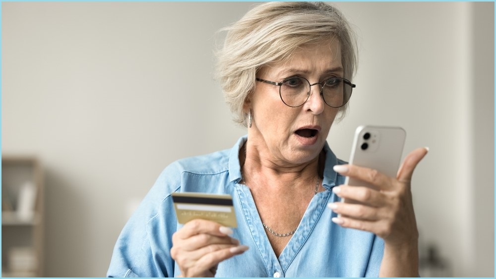 Shocked woman looking at phone screen and holding a credit card.