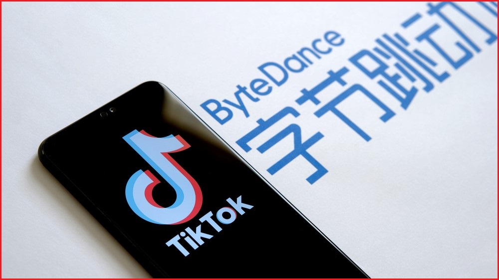 A close up of a mobile phone displaying the TikTok logo, next to a backdrop of the ByteDance logo