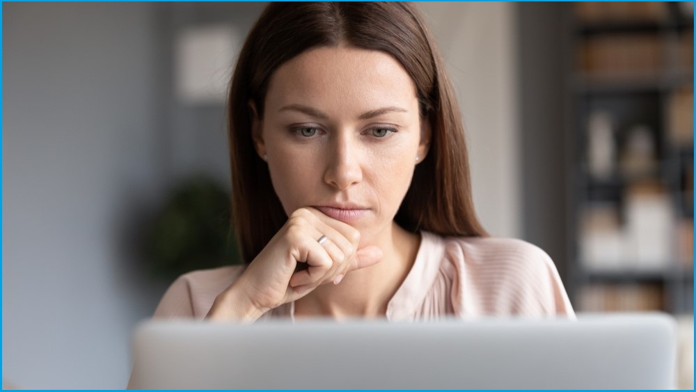 Woman deep in thought looking at a laptop monitor