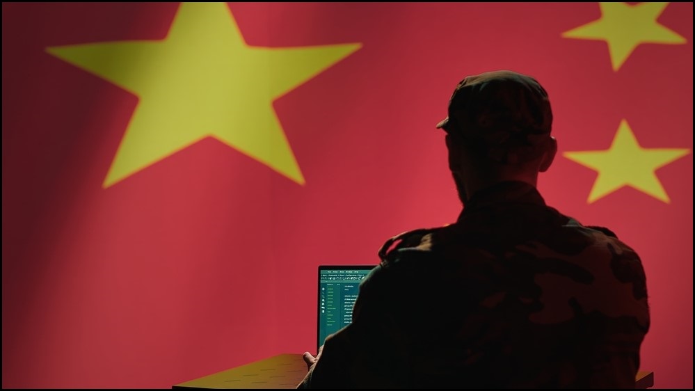 A man working on a computer with a Chinese flag as the backfrop