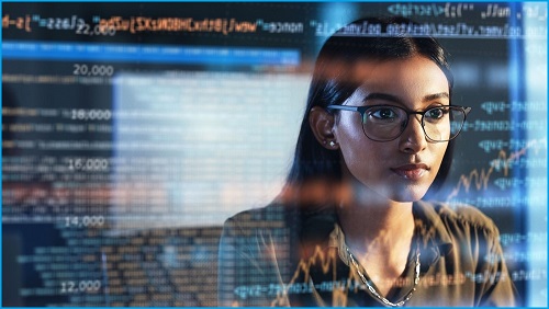 Woman sitting at desk, typing on keyboard and looking at monitors.