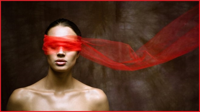 Naked woman  from shoulders up with sheer red scarf wrapped around her eyes.