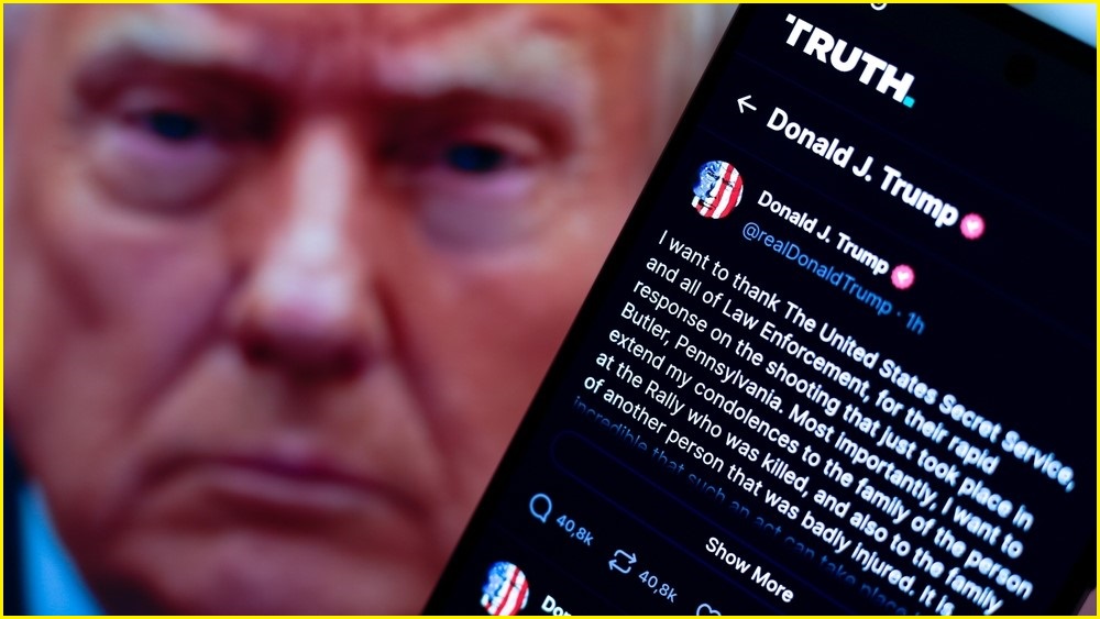 A close up of a phone showing a social media post by Donald Trump. Donald Trump's face in the background.