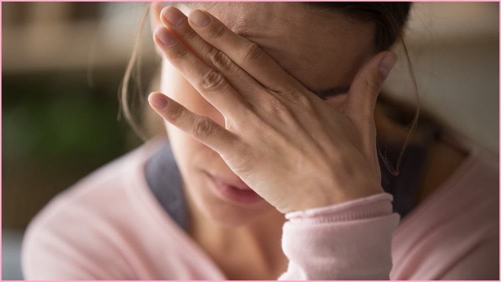 Woman in a pink jumper covering her eyes.