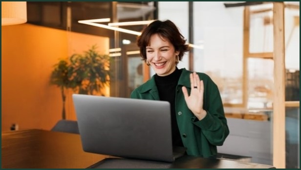 Woman working remotely, waving to a coworker over a video conference call.