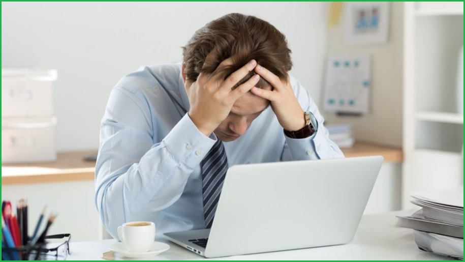 Frustrated man holding his head in his hands, looking at a laptop screen.