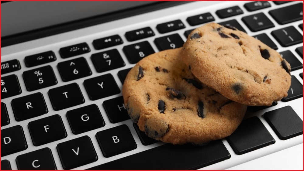 Two chocolate chip cookies resting on a laptop keyboard.