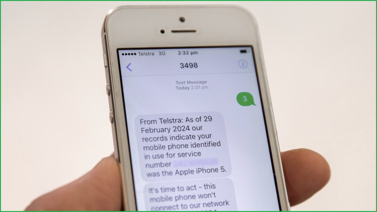 A close up of a hand holding an iPhone 5 displaying text messages about Telstra closing its 3G network.