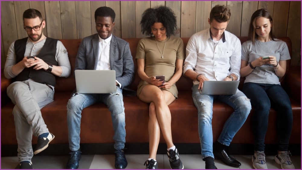Young people sitting on a couch using phones and laptops.