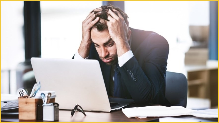 Man looking at laptop screen, holding his head, looking stressed.