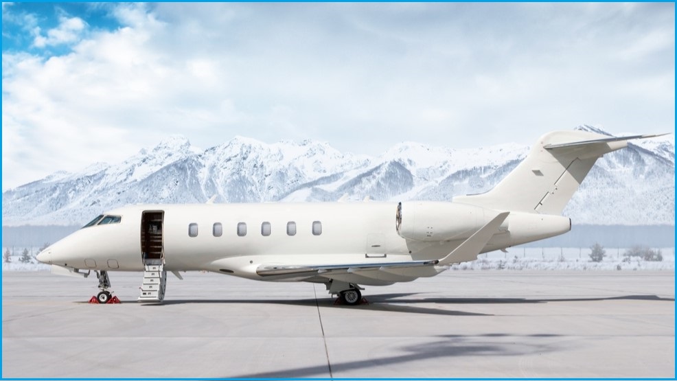 A white private jet on the tarmac with a mountain in the background.