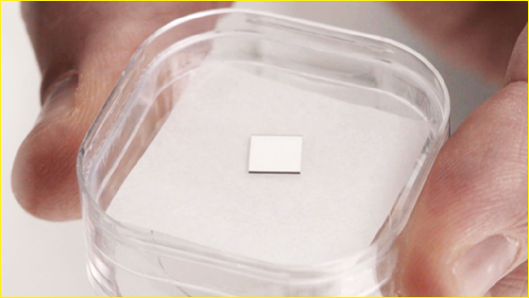 A close up of a quantum diamond chip in a small plastic container, held by a person's fingers.