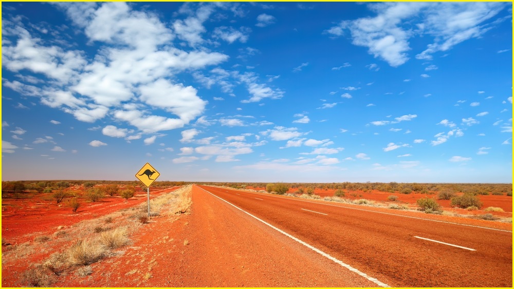 Red dirt road, blue sky with clouds.