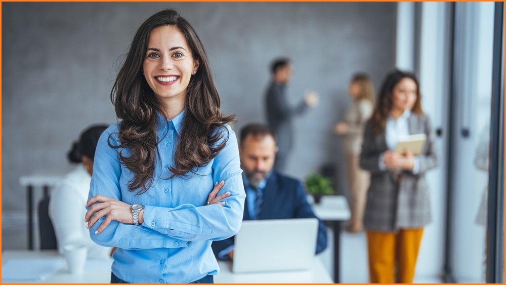 Woman smiling broadly with office colleagues in the background.