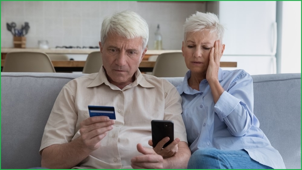 Older couple looking shocked while holding a credit card and looking at a phone screen