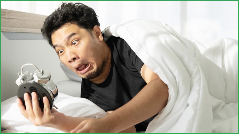 Man waking up shocked holding an alarm clock.