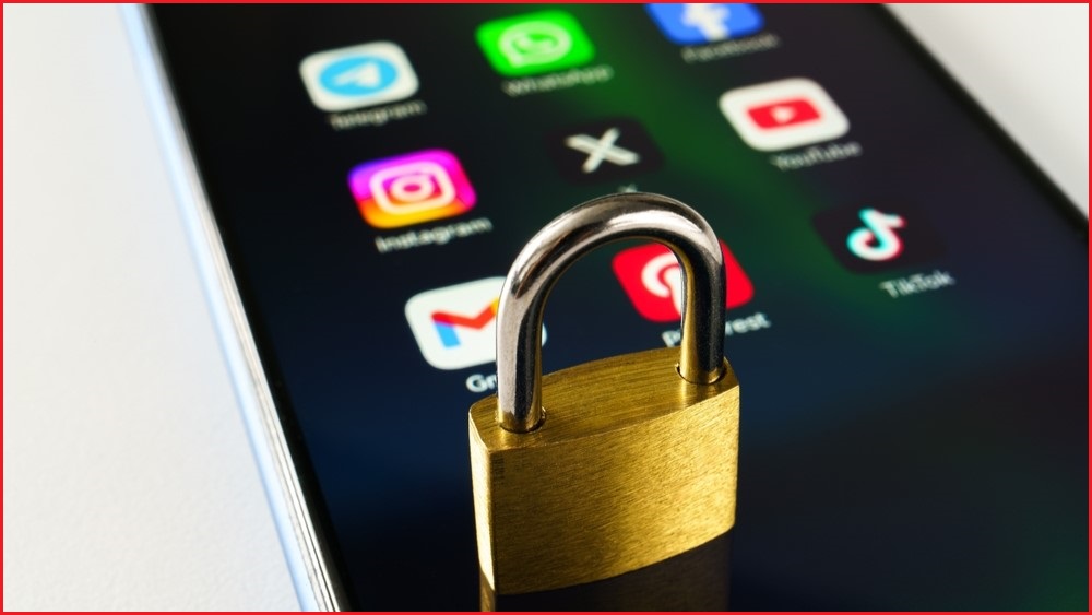 A close up of a small padlock sitting on the screen of a smartphone, which is displaying apps from social media platforms.