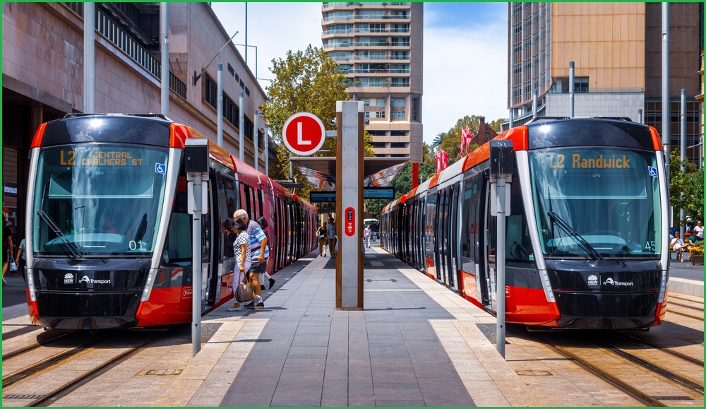 A wide outdoor photo of two light rail trains sitting on either side of a platform in Sydney.