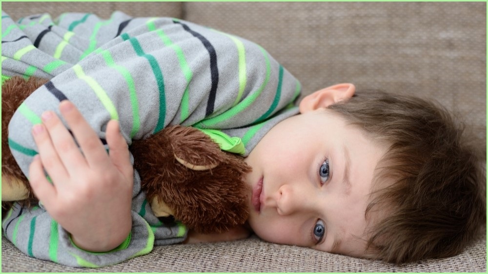 Young boy laying down cudding a stuffed toy.