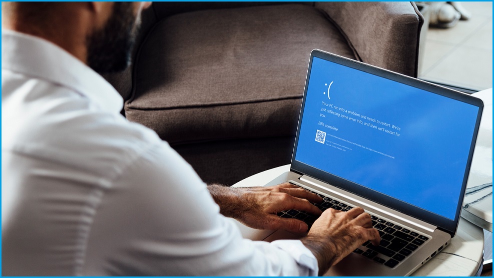 Man using Windows laptop displaying the 'blue screen of death'.